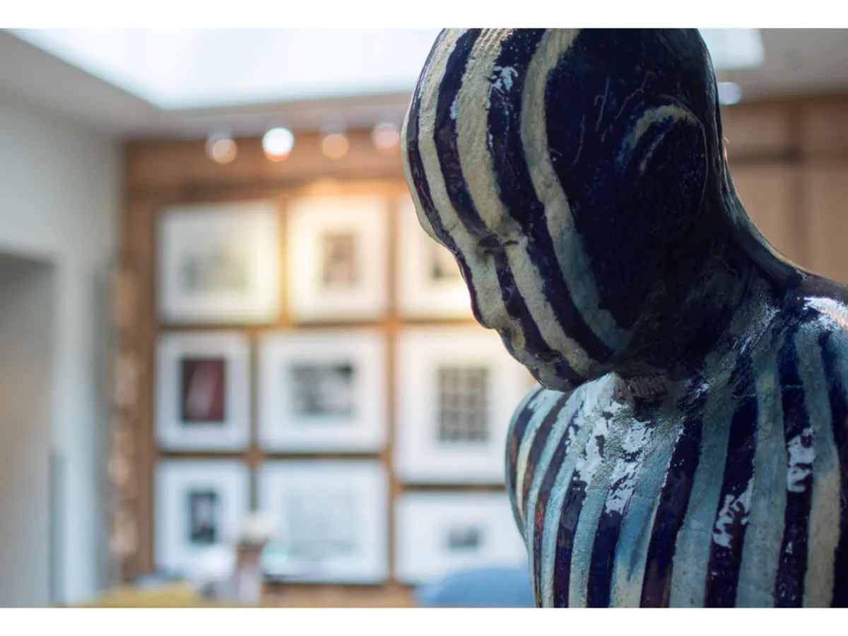 A modern gallery space features a striking striped sculpture and a wall of framed art. The creative setting inspires thoughtful conversation and moments of reflection, with the ambiance hinting at local artistry and community energy.