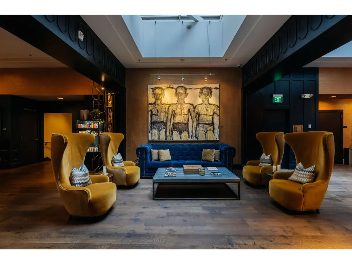A creative, welcoming room with a blue couch, yellow armchairs, a large colorful painting, and a wooden coffee table. The layout encourages both socializing and relaxation, with artistic elements adding a playful, lively mood.