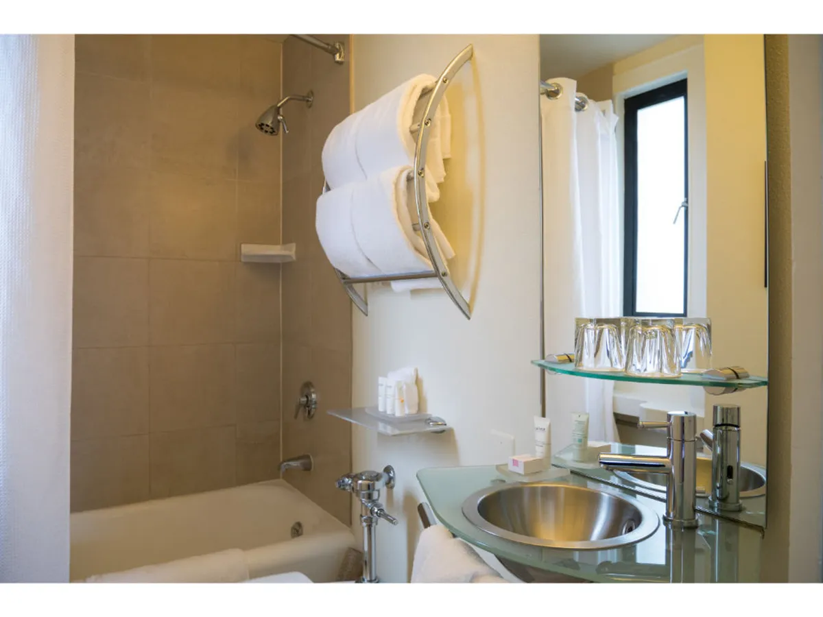 This image features a serene en-suite bathroom with a modern bathtub, sink, towel rack, and mirror, evoking a spa-like, refreshing atmosphere. The setup hints at luxurious bathing and relaxation rituals.
