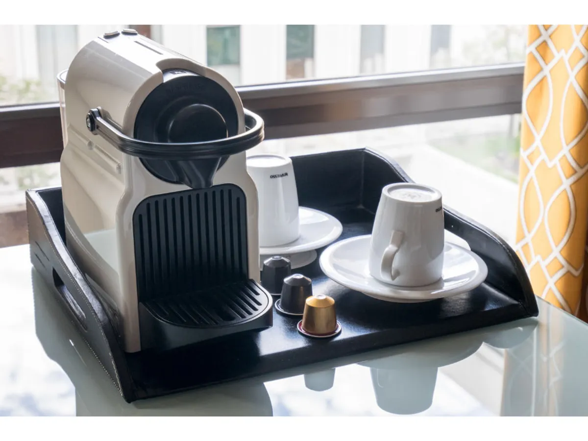 This image centers on the in-room coffee experience with a modern coffee machine, cups, and a tray, set against a cozy backdrop. The scene suggests an inviting morning or afternoon ritual, perfect for savoring Nespresso coffee or Smith Tea.
