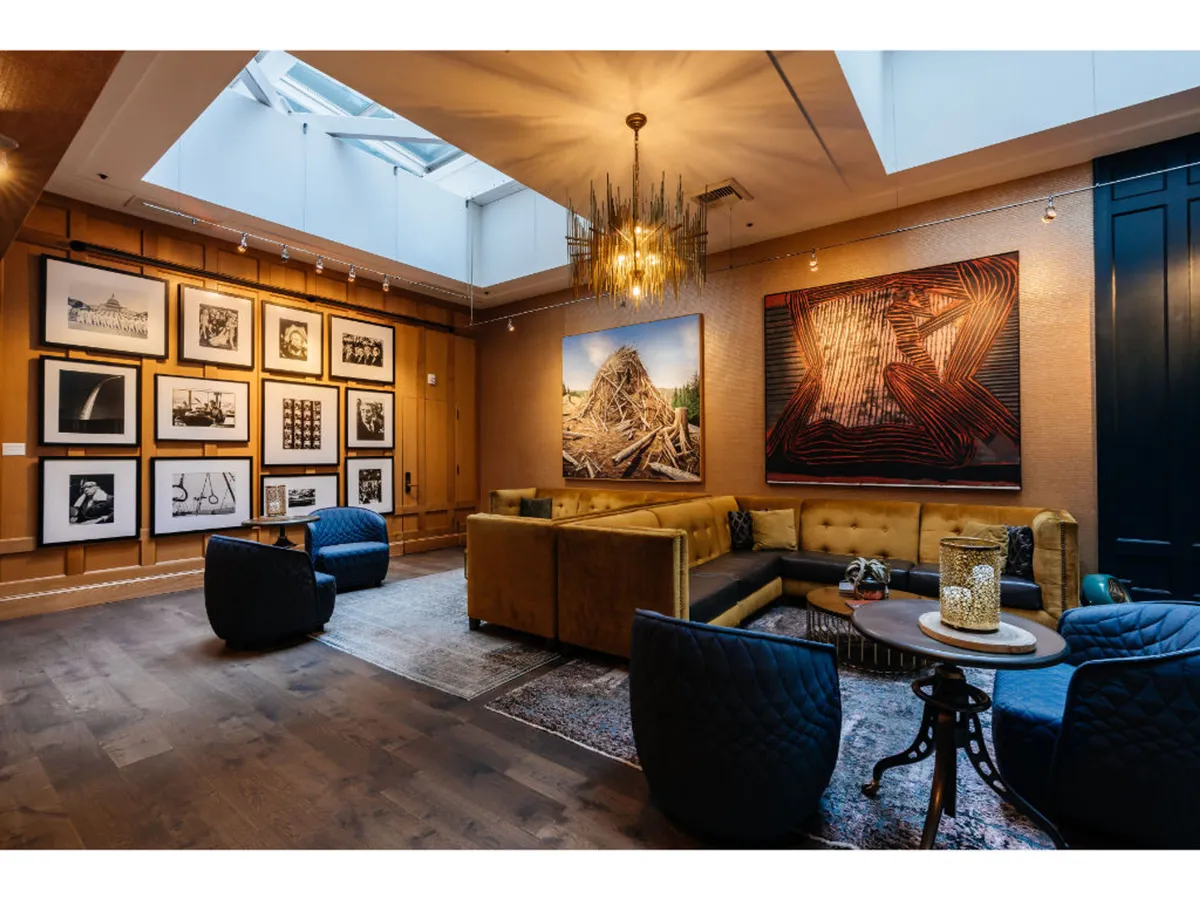 A spacious art-filled public area with large, bold art pieces on the walls, a modern chandelier, and comfortable seating. The arrangement encourages social gatherings and discussion, set against a backdrop of creative energy.
