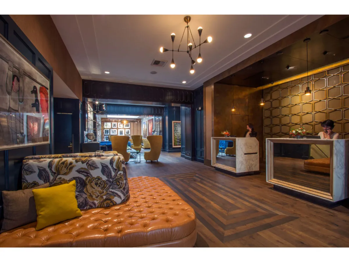 The inviting hotel lobby features a tufted orange sofa, artistic wall decor, and unique lighting fixtures, creating a warm welcome upon arrival. Guests can be seen socializing, reading, or waiting for check-in, which hints at the smooth hospitality and attentive service mentioned in the section.
