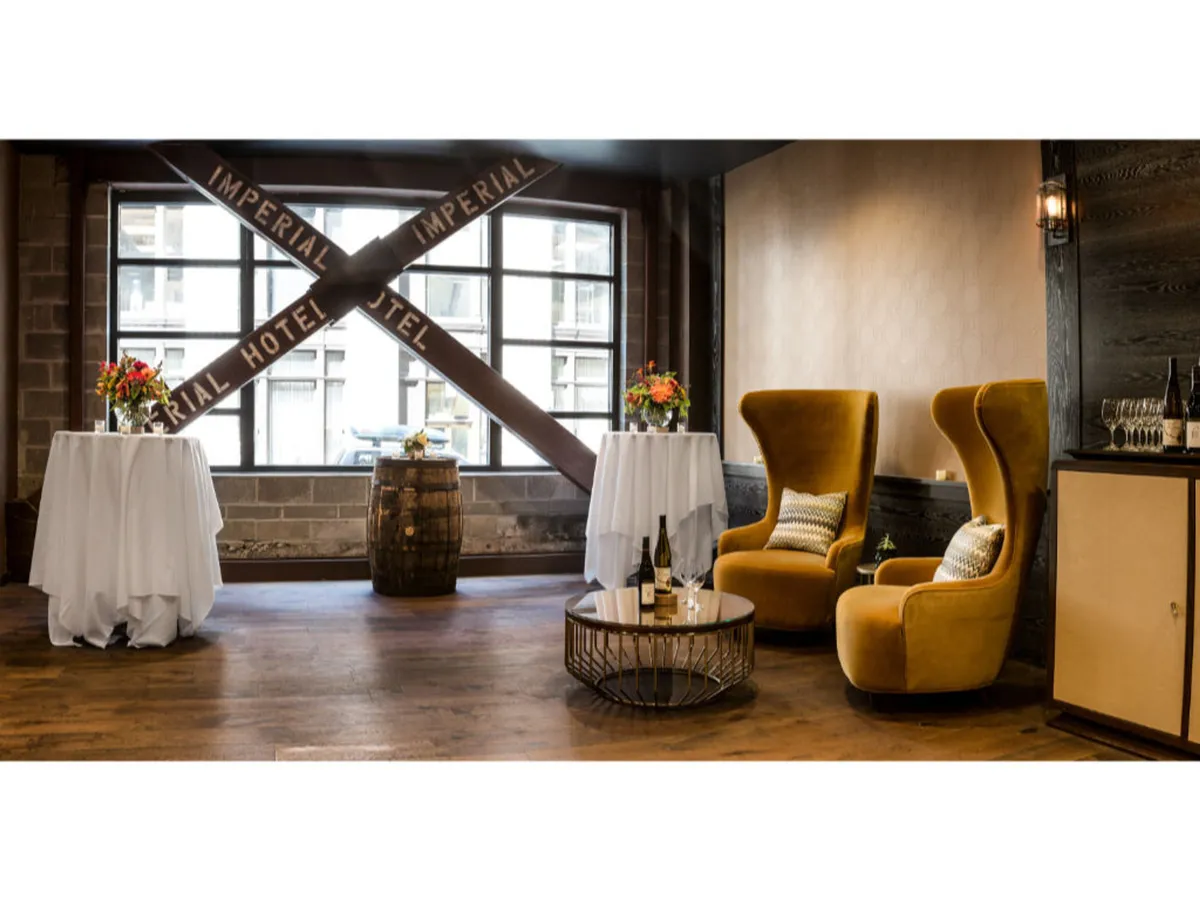A pair of inviting yellow armchairs sit beside round tables draped in crisp white tablecloths, with a decorative barrel and coffee table adding character. The layout suggests a sophisticated lounge or shared space, ideal for relaxing after a city adventure.