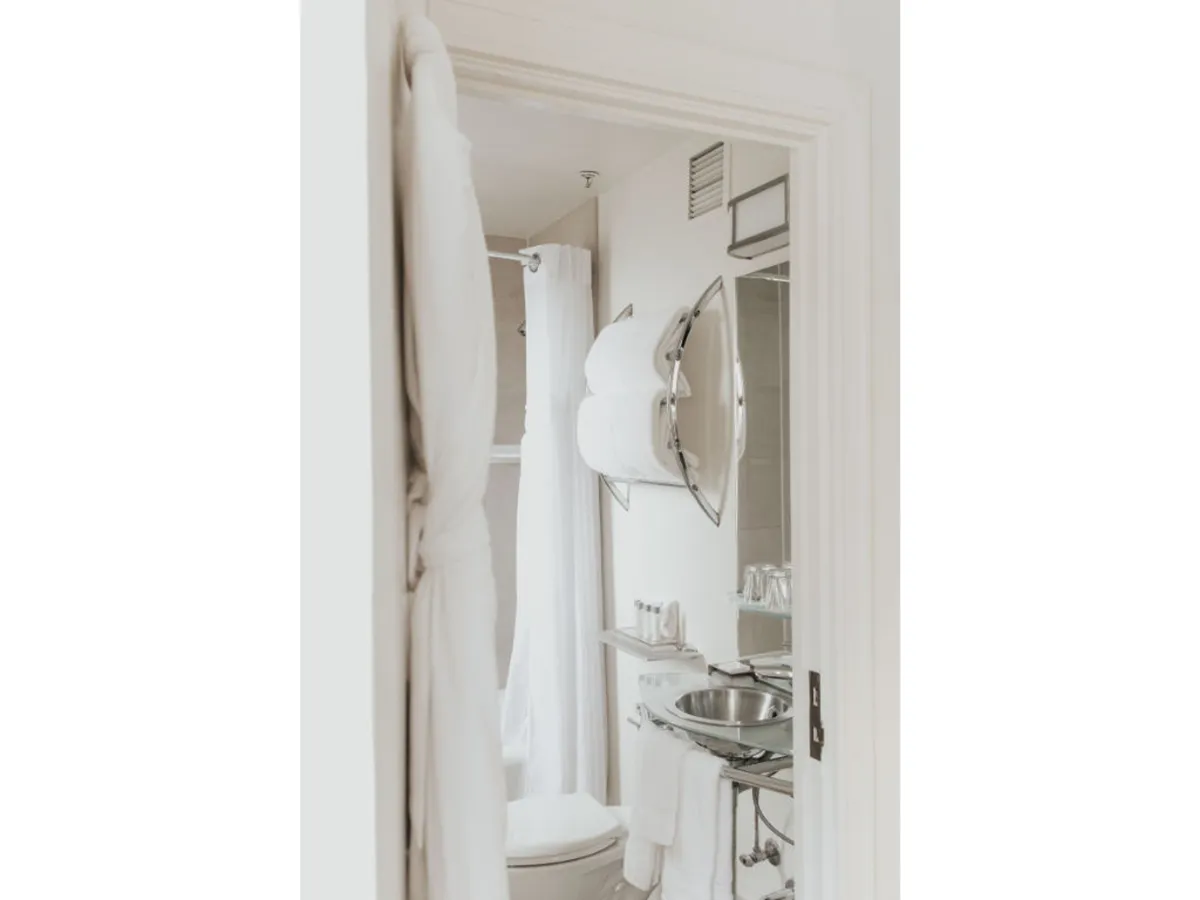 A tranquil bathroom scene with a well-appointed vanity, mirror, towels, and a shower curtain, evoking a spa-like atmosphere. The space is clean, fresh, and ready for guests to enjoy personal care routines or take advantage of daily housekeeping service.