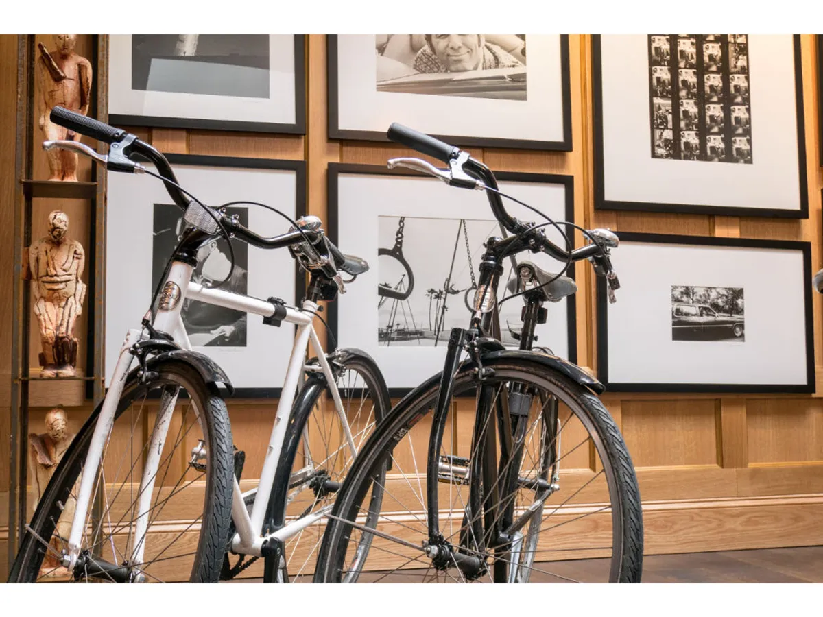 An interior scene featuring a stylish lineup of bicycles ready for use, set against a backdrop of artful photographs and warm wood paneling. The space buzzes with creative energy and hints at the hotel’s bicycle rental amenity.